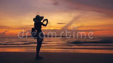 海洋海滩日落时分，戴帽子的年轻游客女士用<strong>手机</strong>拍照<strong>剪影</strong>